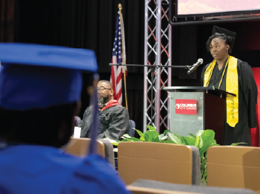 student standing on stage in cap and gown